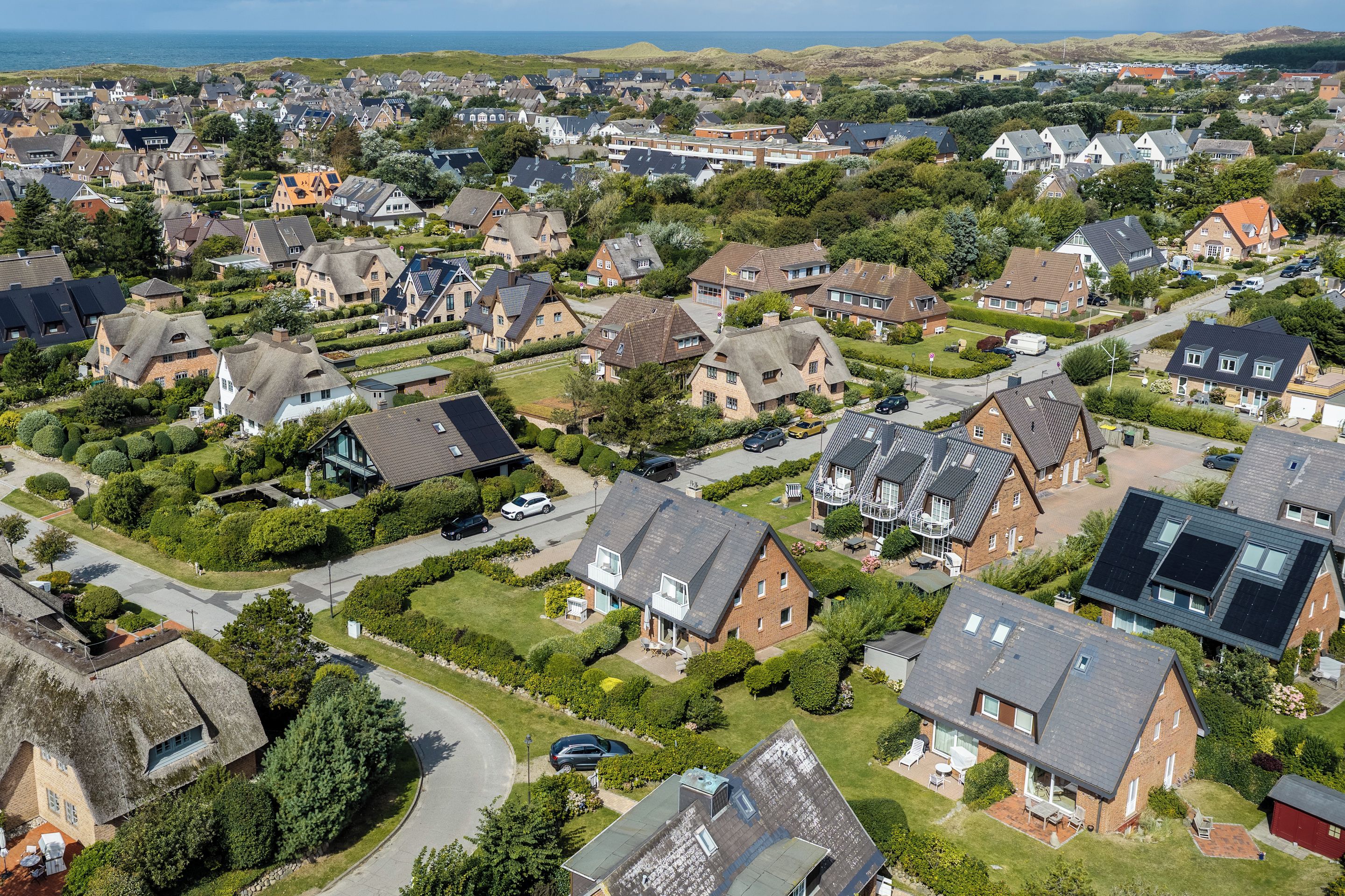 A residential area with houses, some with sloped roofs and others with flat roofs, surrounded by greenery and a clear sky.