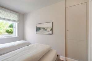 A bedroom with a bed, a window with a view of greenery, and a wardrobe. - Your modern retreat in Wenningstedt. (Wenningstedt-Braderup (Sylt))