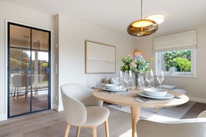 A dining area with a round table, chairs, and a vase with flowers. - Your modern retreat in Wenningstedt. (Wenningstedt-Braderup (Sylt))