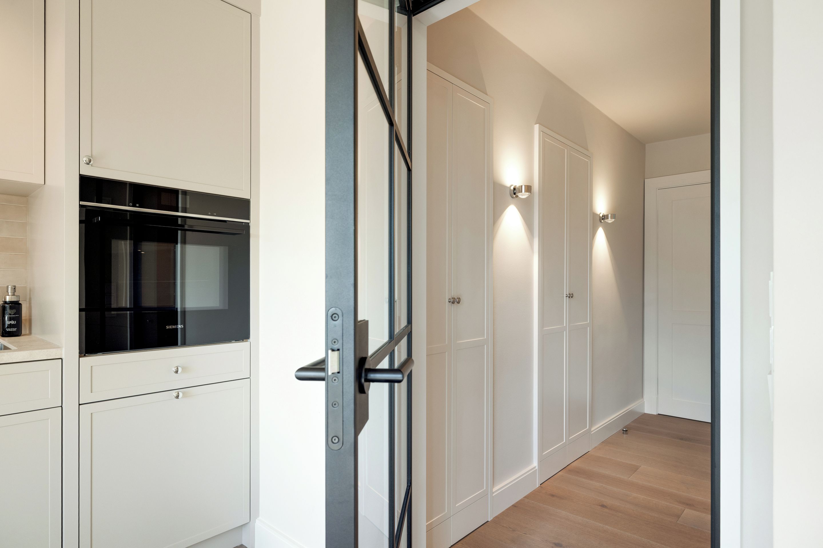A modern kitchen with white cabinetry, a black oven, and a wooden floor.