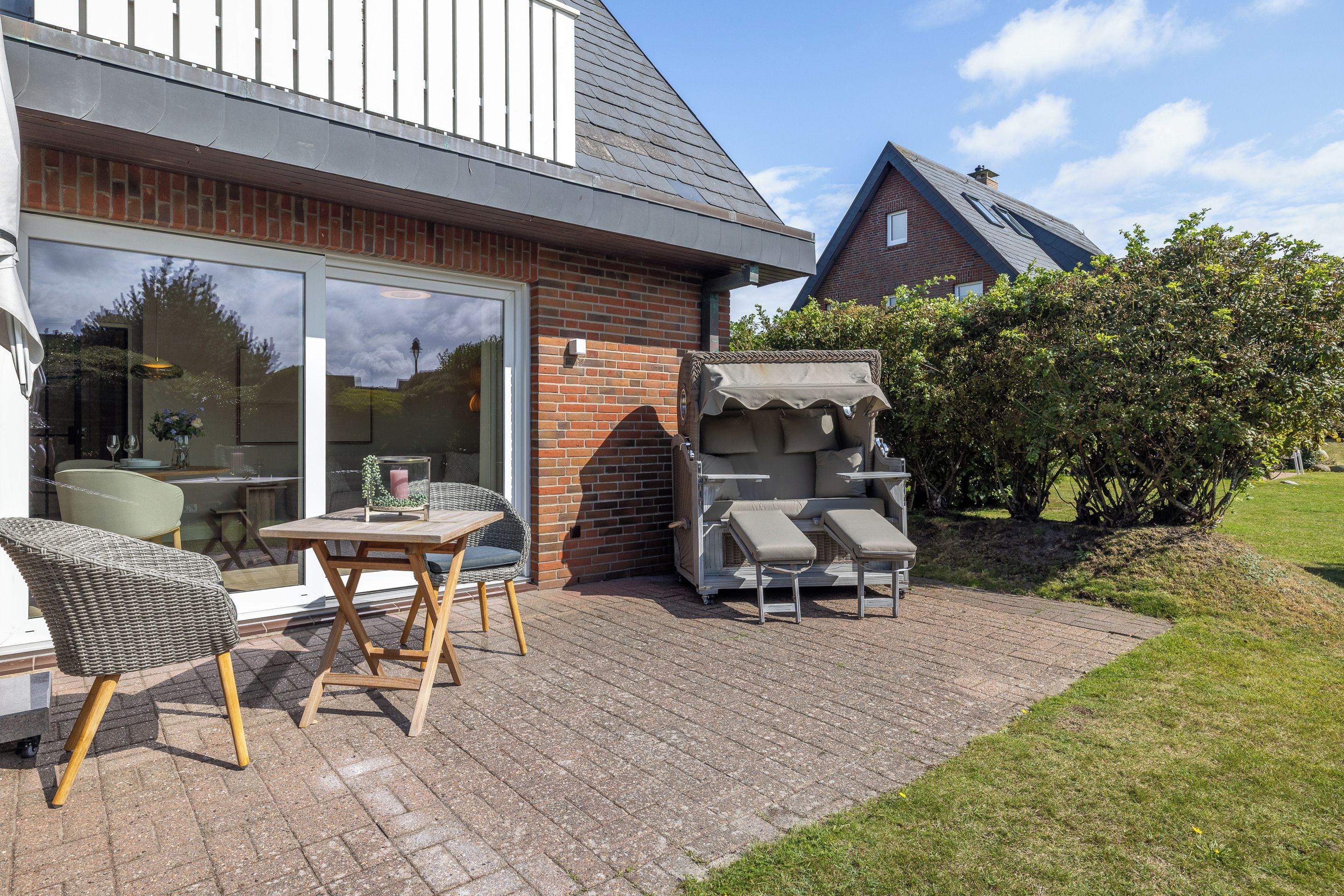 Een terras met buitenmeubilair, een barbecue en een glazen deur naar een kamer.