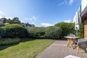 Een terras met een tafel en stoelen, omgeven door een verzorgde haag en een gazon.