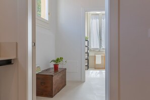 A hallway with a wooden chest of drawers, a potted plant, and a view into a room with a window and curtains. - A modern 120 sqm apt located on the third floor of a period building, it is equipped with every comfort to comfortably host two adults and a child.The apartment is located in a centrally located area (ZTL in Italian), less than 160 mt from Torresotto di  (Bologna)