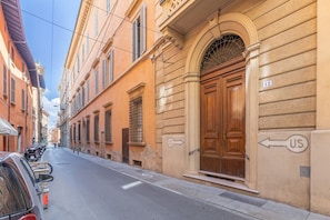 A street view with a building featuring a large wooden door, a number '12' sign, and a U.S. directional sign. - A modern 120 sqm apt located on the third floor of a period building, it is equipped with every comfort to comfortably host two adults and a child.The apartment is located in a centrally located area (ZTL in Italian), less than 160 mt from Torresotto di  (Bologna)