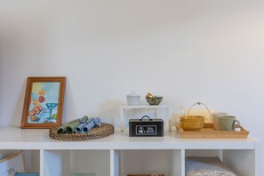 Ein weißes Regal mit einem gerahmten Gemälde, einer Aufbewahrungsbox für Teebeutel und einer Holztablett mit Schalen und einer Tasse.