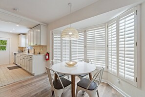 A modern kitchen with white cabinets, a dining area with a round table and chairs, and large windows with white shutters. - Singer Island Sanctuary (Palm Beach Shores)