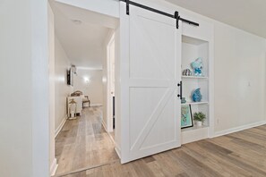 Un pasillo con una puerta corredera blanca que da a una habitación con estanterías y objetos decorativos.