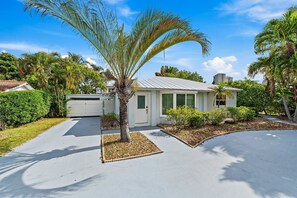A residential house with a driveway, palm tree, and surrounding greenery. - Singer Island Sanctuary (Palm Beach Shores)