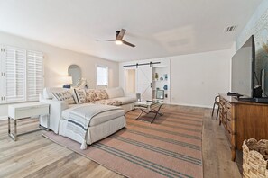 A spacious living room with a sofa, a coffee table, a TV, and a ceiling fan. - Singer Island Sanctuary (Palm Beach Shores)