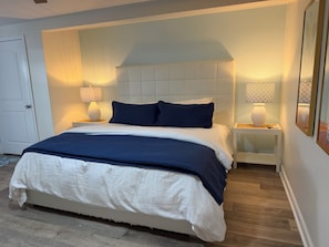 A bedroom with a bed, bedside lamps, a nightstand, and a framed picture on the wall. - Singer Island Sanctuary (Palm Beach Shores)