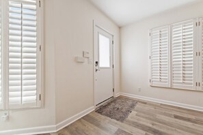 A room with a door, a window with blinds, a wall-mounted thermostat, and a patterned rug on a wooden floor. - Singer Island Sanctuary (Palm Beach Shores)