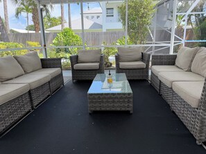 Een overdekt terras met rieten meubels en een glazen salontafel.