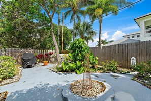 A backyard with a wooden fence, a barbecue grill, and various plants. - Singer Island Sanctuary (Palm Beach Shores)