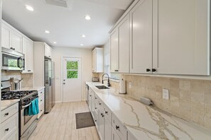 A modern kitchen with white cabinets, a marble countertop, and a built-in microwave. - Singer Island Sanctuary (Palm Beach Shores)