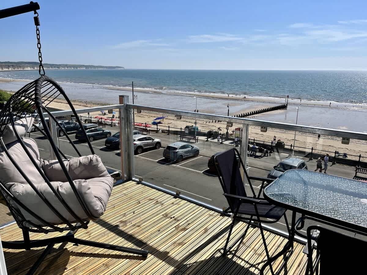 Een balkon met een hangstoel, een tafel en uitzicht op strand en zee.
