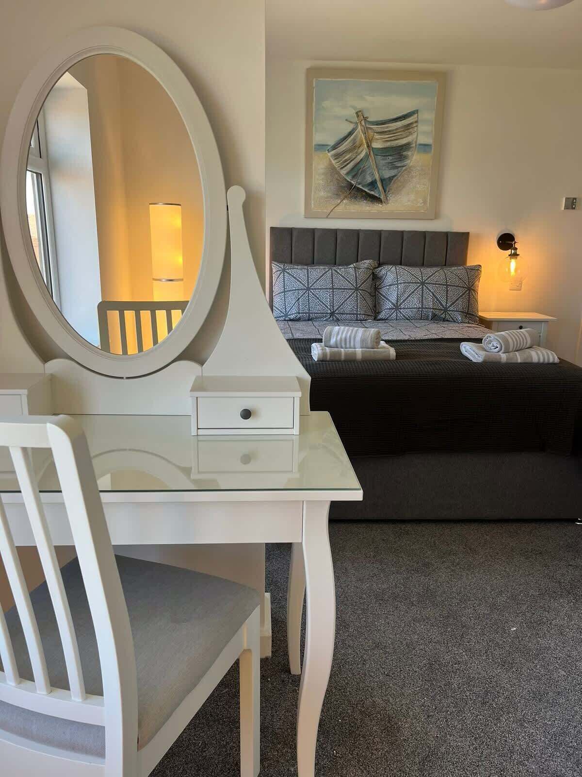 A bedroom with a bed, a bedside table, a chair, a round mirror, and a painting on the wall.