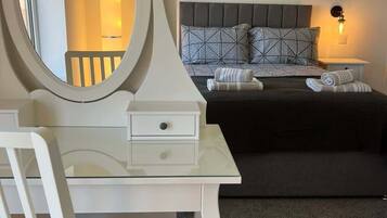 A bedroom with a bed, a bedside table, a chair, a round mirror, and a painting on the wall.