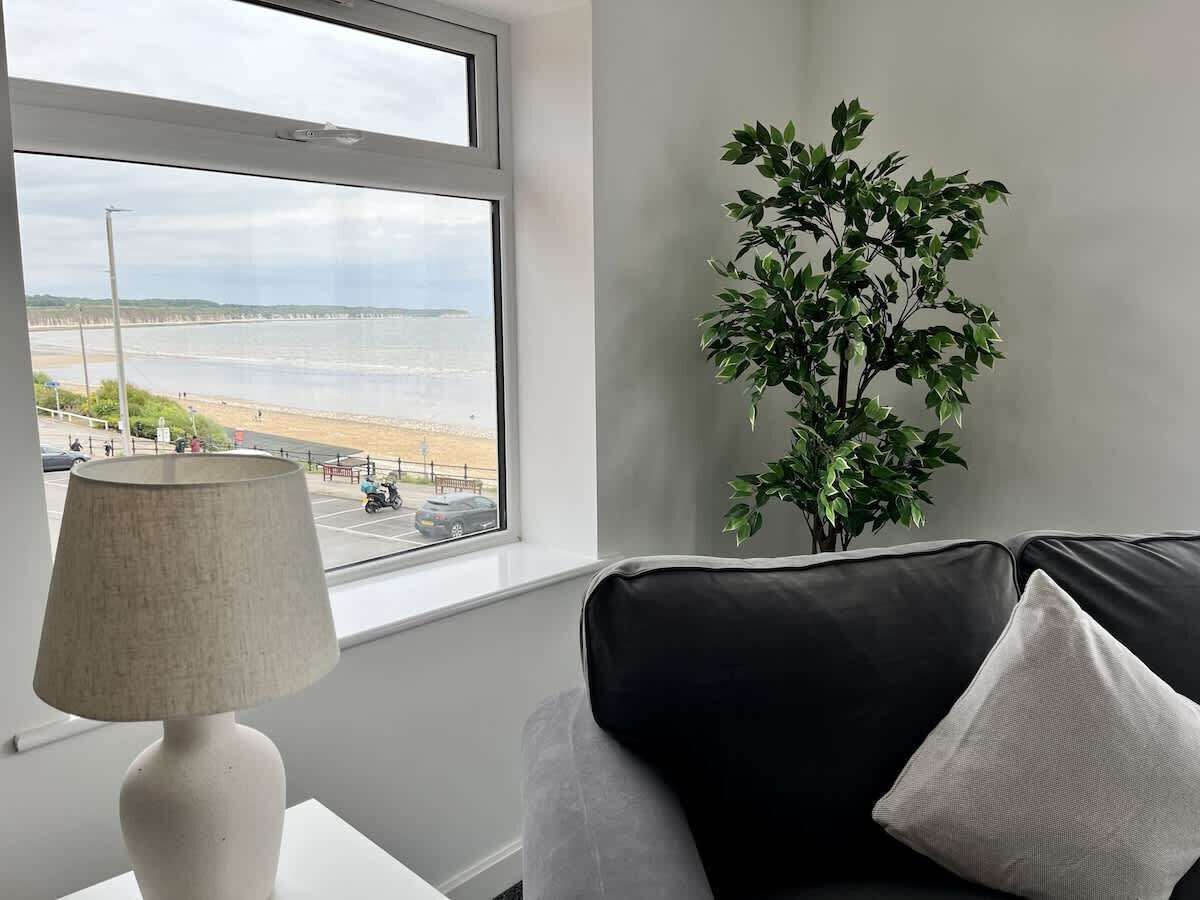 Una habitación con ventana que da a una playa, una lámpara y una planta.