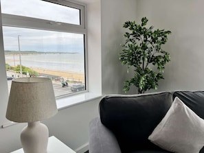 Una habitación con ventana que da a una playa, una lámpara y una planta.