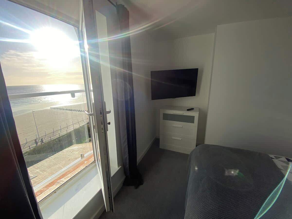 A hotel room with a bed, a television on the wall, and a window with a view of the sea.