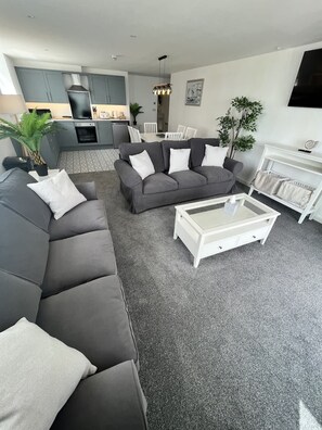 Una sala de estar moderna con un sofá seccional gris, una mesa de centro blanca y un comedor con una mesa y sillas blancas.
