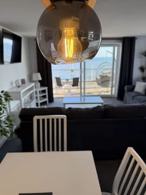 Ein modernes Wohnzimmer mit Essbereich, einem großen Fenster und einem Ausblick sowie einer ungewöhnlichen, kugelförmigen Leuchte.