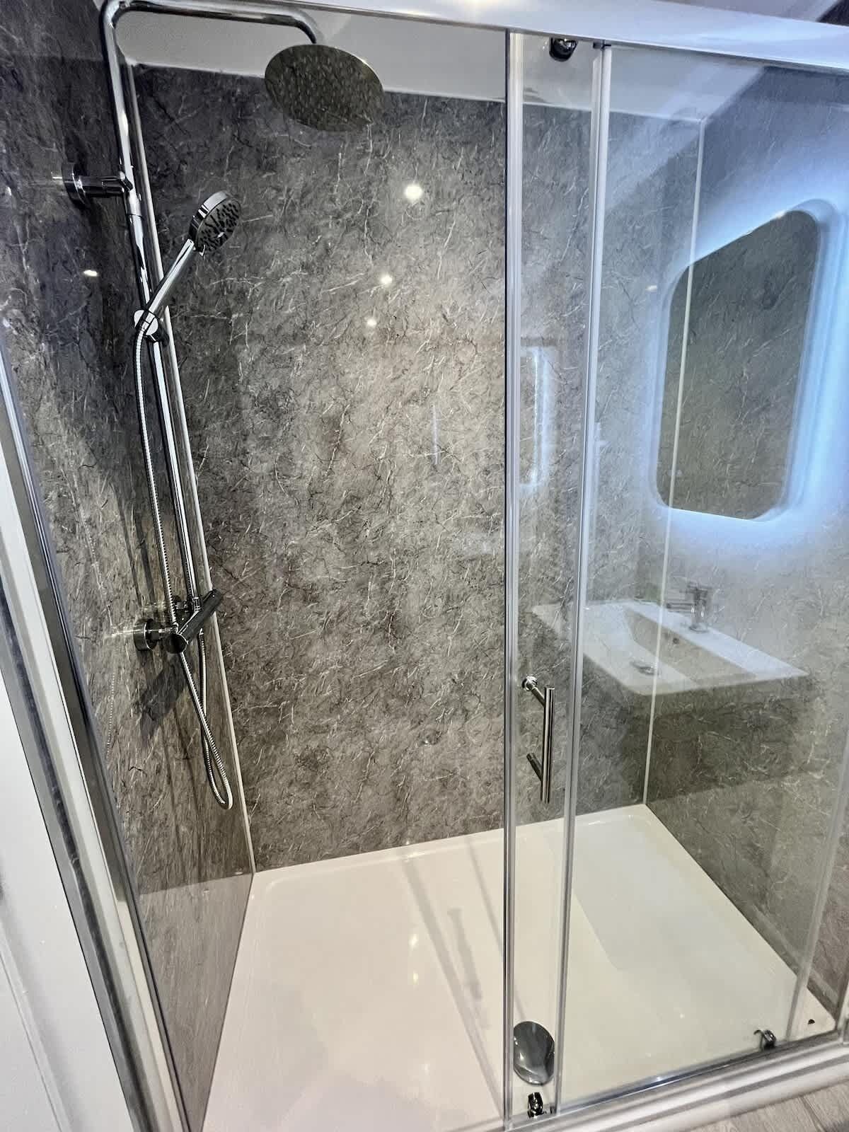 A modern bathroom with a glass-enclosed shower, a white bathtub, and a marble wall.