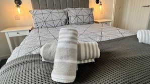 Um quarto com uma cama, duas mesas de cabeceira, uma luminária na parede e um quadro.