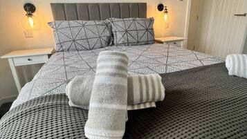 Un dormitorio con una cama, dos mesitas de noche, una lámpara de pared y un cuadro.