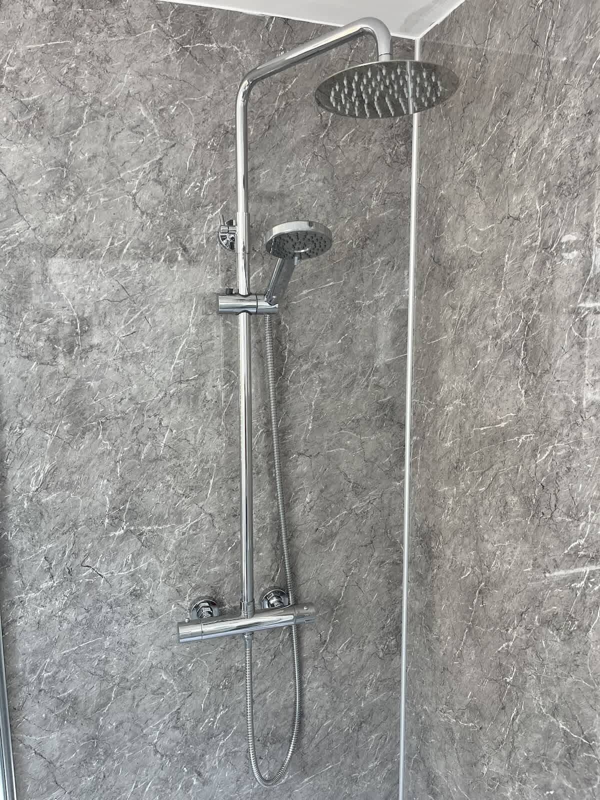 Ducha moderna con cabezal de ducha manual y cabezal de ducha de lluvia fijo, montada en una pared de textura similar al mármol.