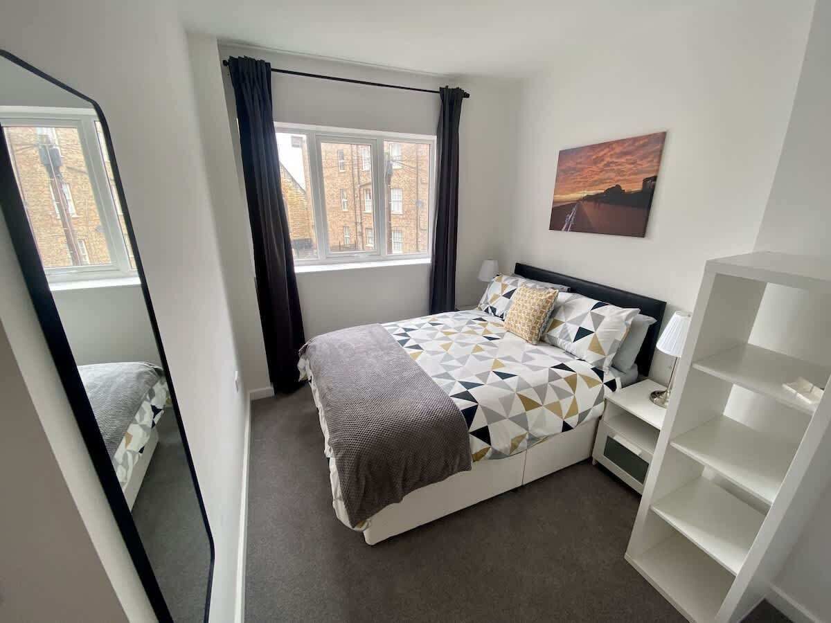 A bedroom with a bed, a window, a nightstand, and a bookshelf.