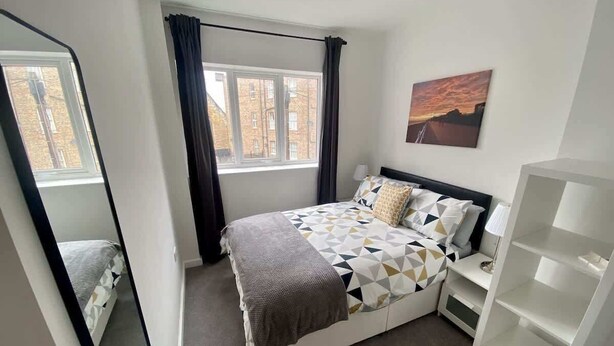 Un dormitorio con cama, ventana, mesita de noche y estantería.