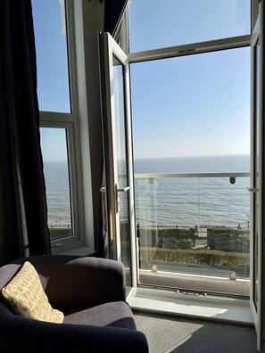 Ein Zimmer mit großem Fenster mit Blick auf ein Gewässer, einem Sofa mit Kissen und einer Ansicht der fernen Küste.