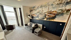 Una sala de estar con un sofá, una mesita y un cuadro de barcos en la pared.
