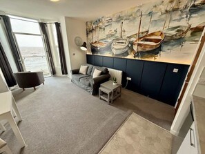 Ein Wohnzimmer mit einer Couch, einem kleinen Tisch und einem Gemälde von Booten an der Wand.