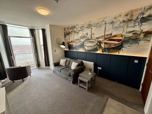 A living room with a sofa, a small table, and a painting of boats on the wall. - Bridlington Bay Apt. 4 (East Riding of Yorkshire)