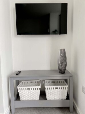 A flat-screen TV mounted on a wall above a grey console table with two white baskets and a vase. - Bridlington Bay Apt. 4 (East Riding of Yorkshire)