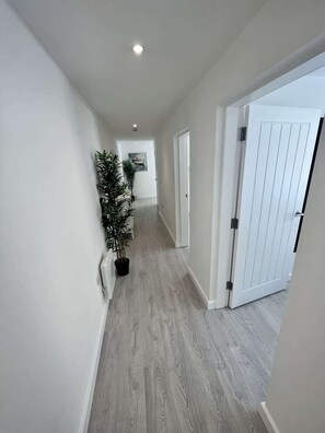 A hallway with a wooden floor, white walls, and a door on the right. - Seaside Escapes Apt. 1 (East Riding of Yorkshire)