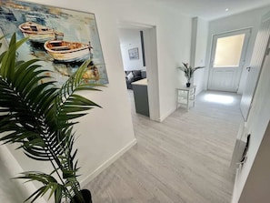 Un couloir avec un plancher en bois, un tableau représentant des bateaux et une plante en pot.