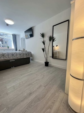 A modern bedroom with a large bed, a flat-screen TV, a potted plant, and a mirror. - Seaside Escapes Apt. 1 (East Riding of Yorkshire)
