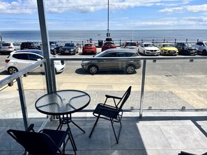 A view from a balcony overlooking a parking lot with several cars, a glass table, and chairs. - Seaside Escapes Apt. 1 (East Riding of Yorkshire)