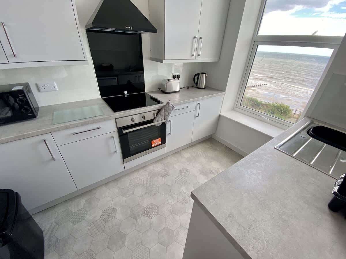 A modern kitchen with white cabinets, a black range hood, a toaster, and a kettle.