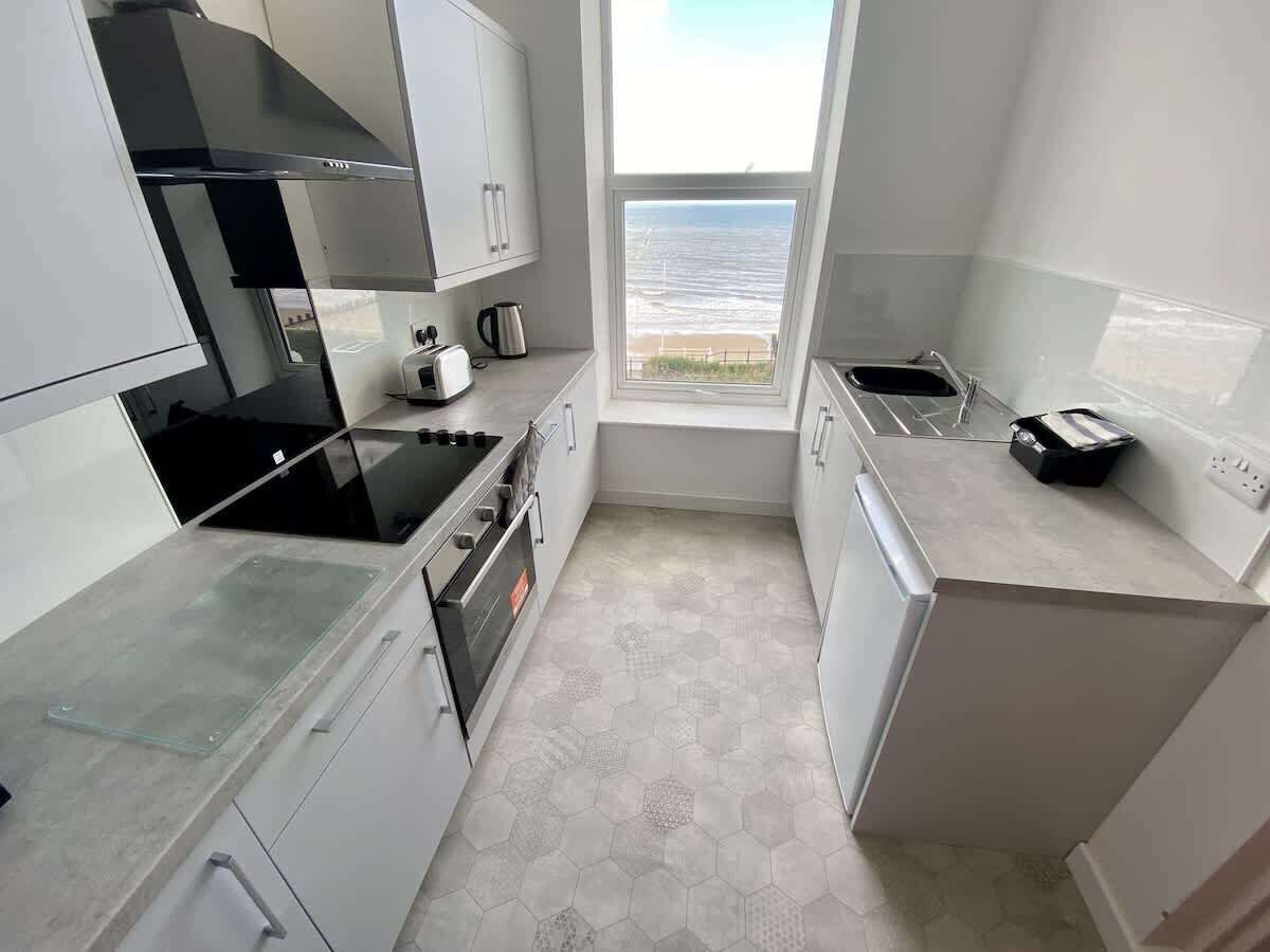 A compact kitchen with a view of the sea, featuring a stove, oven, and modern appliances.