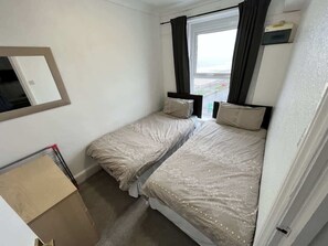 A room with two beds, a window with curtains, a small mirror, and a cart. - Harbour View Apt, Oceana (East Riding of Yorkshire)