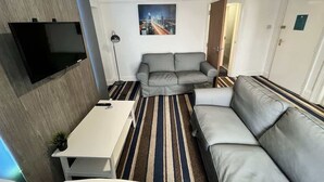 A compact living space with a sofa, a small table, a flat-screen TV mounted on the wall, and a striped rug. - Harbour View Apt, Oceana (East Riding of Yorkshire)