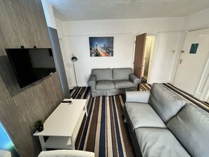 A compact living space with a sofa, a small table, a flat-screen TV mounted on the wall, and a striped rug. - Harbour View Apt, Oceana (East Riding of Yorkshire)