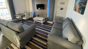 A modern living room with a flat-screen TV mounted on a wall, a striped rug, and two grey sofas. - Harbour View Apt, Oceana (East Riding of Yorkshire)