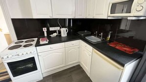 A compact kitchen with white cabinetry, a black countertop, a microwave, a stove, and a sink. - Harbour View Apt, Oceana (East Riding of Yorkshire)