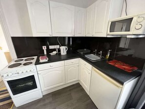 A compact kitchen with white cabinetry, a black countertop, a microwave, a stove, and a sink. - Harbour View Apt, Oceana (East Riding of Yorkshire)