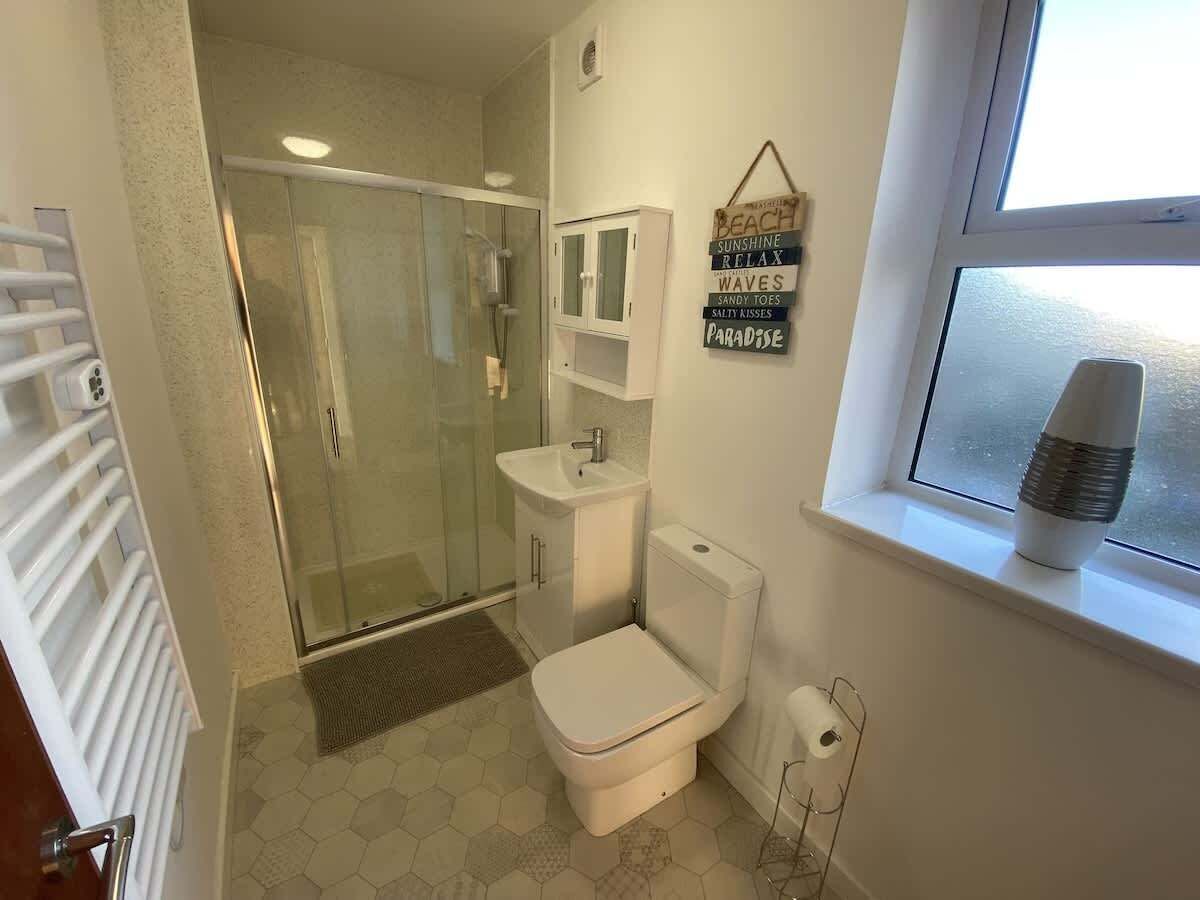 A bathroom with a glass-enclosed shower, a toilet, a sink, and a window with a view.